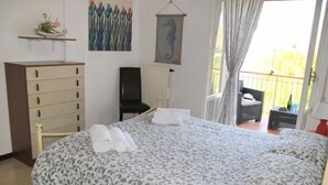 Un dormitorio con cama, una silla, un aparador y un balcón con una silla.