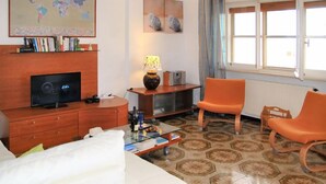 Una habitación de hotel con televisión, un mapa, una lámpara, dos sillas naranjas y una cama.