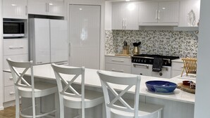 A modern kitchen with white cabinetry, a central island with bar stools, a microwave, and a stove. - Bargara - Everday's a Holiday! (Bargara)