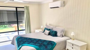 A bedroom with a bed, nightstands, a lamp, and an air conditioning unit. - Bargara - Everday's a Holiday! (Bargara)