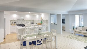 A modern kitchen with white cabinets, a dining area with white chairs and a table, and a living room with a sofa and a TV. - Bargara - Everday's a Holiday! (Bargara)
