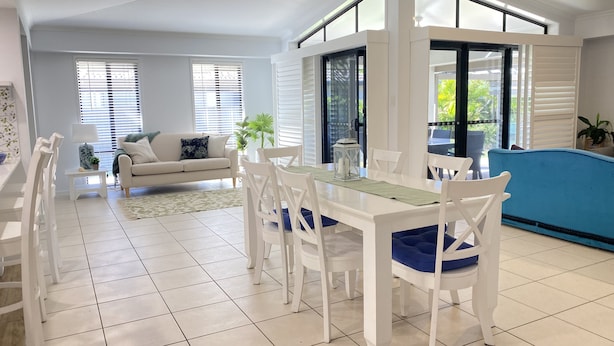 A spacious living area with a dining table, white chairs, a sofa, and a blue accent chair. - Bargara - Everday's a Holiday! (Bargara)