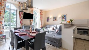 Una sala de estar moderna con comedor, sofá gris, televisor de pantalla plana, obras de arte y una cocina con horno empotrado.