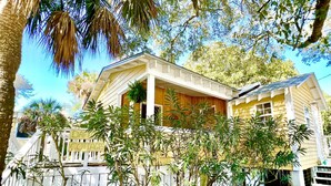 A yellow house with a porch, surrounded by a wooden fence and various plants. - Charming Folly Cottage! Steps to Downtown, Pier & Beach! (Folly Beach)