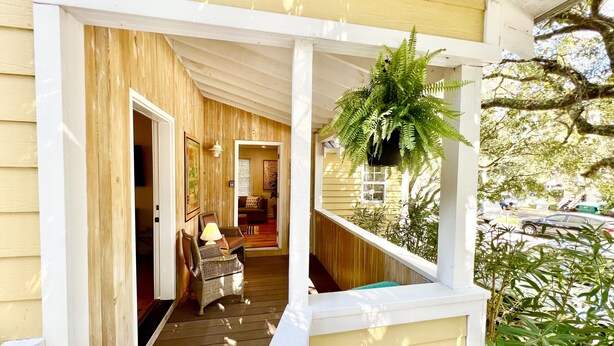 A wooden porch with a hanging plant, a wicker chair, and a lamp. - Charming Folly Cottage! Steps to Downtown, Pier & Beach! (Folly Beach)