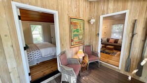A cozy cabin with a loft bedroom, a dining area with wicker furniture, and a living room with a sofa and cushions. - Charming Folly Cottage! Steps to Downtown, Pier & Beach! (Folly Beach)