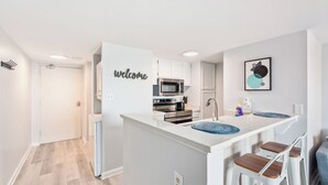 A modern kitchen with white cabinetry, a built-in microwave, and a welcome sign.