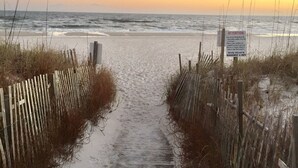 A wooden pathway leading to a beach with a sign indicating beach access rules.