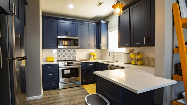 Una cocina moderna con armarios azul oscuro, electrodomésticos de acero inoxidable y encimera blanca.