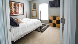 Un dormitorio con cama, ventana, televisor y espacio de almacenamiento.