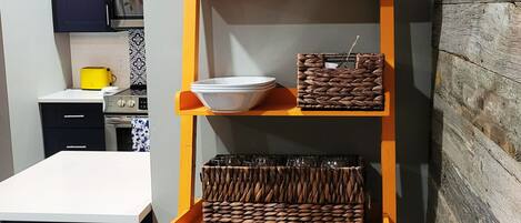 A kitchen with a white countertop, a microwave, and a toaster. There is a wooden shelf with baskets and bowls.