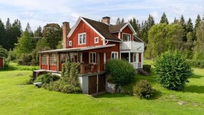 A two-story red house with a large front porch and a covered patio area. - Vacation home Hultet by Interhome (Mullsjö)