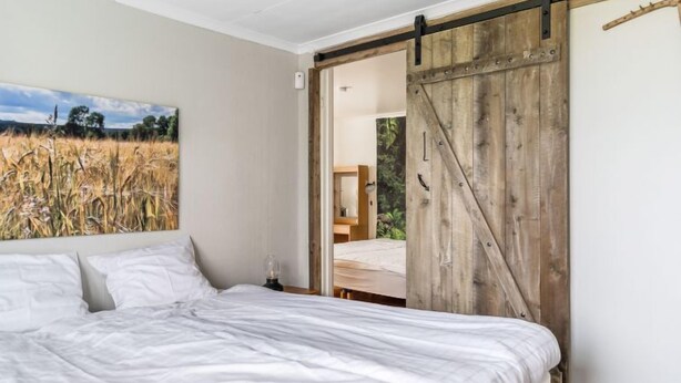 A bedroom with a bed, a sliding barn door, a painting of a field, and a nightstand with a lamp. - Vacation home Hultet by Interhome (Mullsjö)