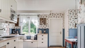 A kitchen with white cabinets, a window seat, and a dining area with blue chairs. - Vacation home Hultet by Interhome (Mullsjö)