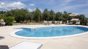 Una piscina amb gandules i ombrelles, envoltada d'arbres i un cel serè.