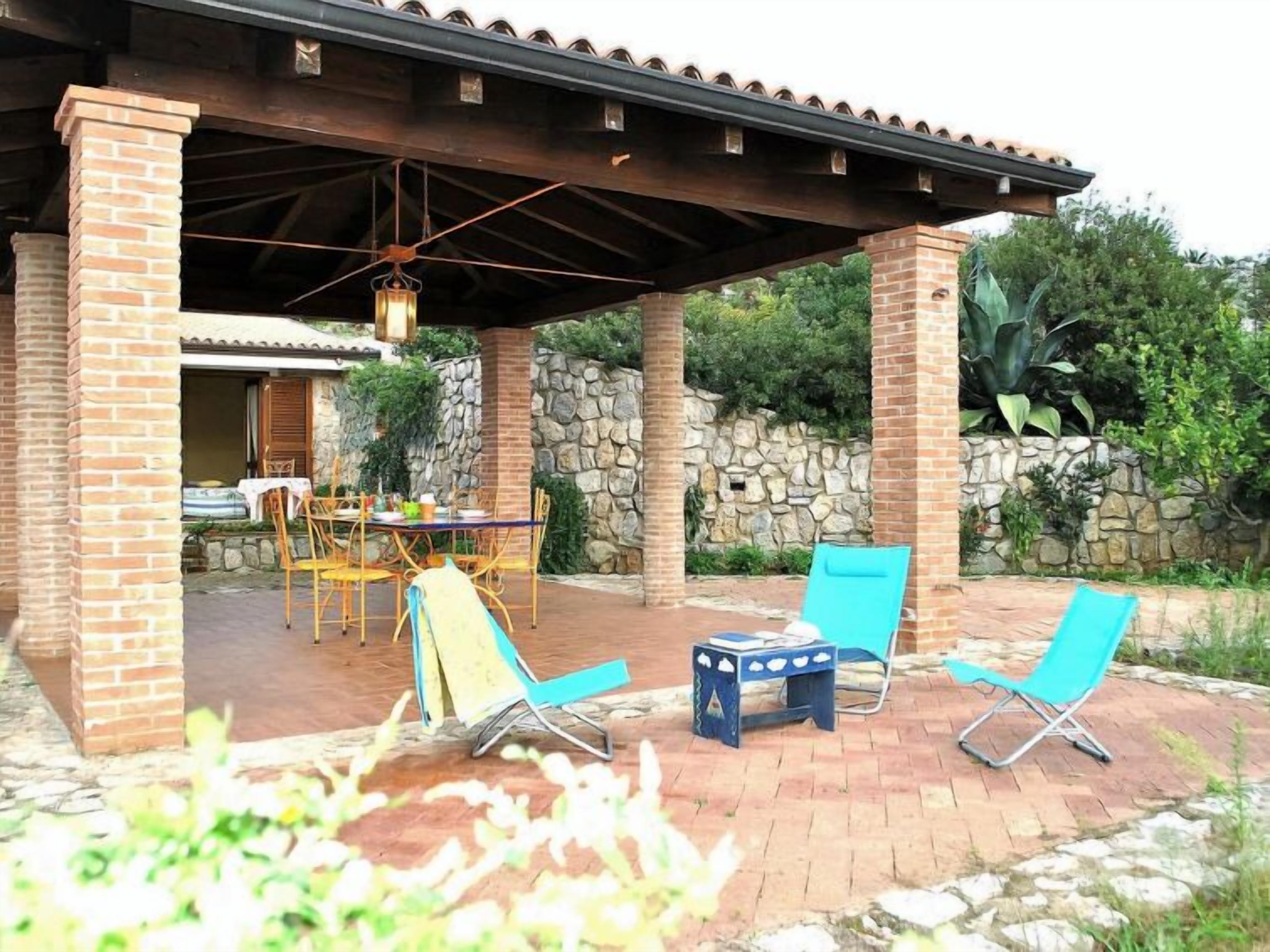 An outdoor patio with a brick table and chairs, a hanging lantern, and a stone wall backdrop.