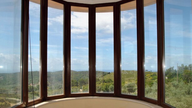 Una habitació amb un gran finestral panoràmic que ofereix vistes de paisatge amb zones de turons.