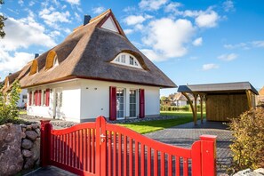 A traditional house with a thatched roof, a red gate, and a wooden structure in the background.