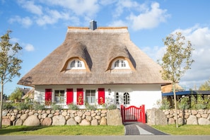 A traditional house with a thatched roof, red shutters, and a stone wall surrounding the property.
