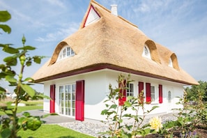 Une maison traditionnelle avec un toit de chaume, des murs blancs et des volets rouges.