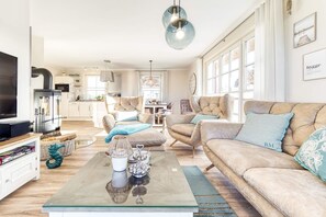 A modern living room with a sofa, armchairs, a glass coffee table, and a TV.