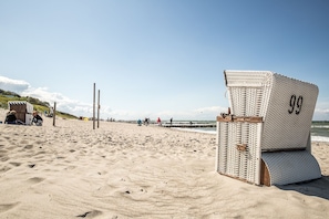 Une plage avec une chaise en osier portant le numéro « 99 » et une structure en bois dans le sable.