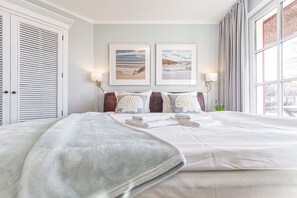 A neatly made bed with towels, two framed artworks above it, and a large window with curtains.