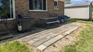 Patio trasero con una parrilla, mesa de picnic y mobiliario exterior.