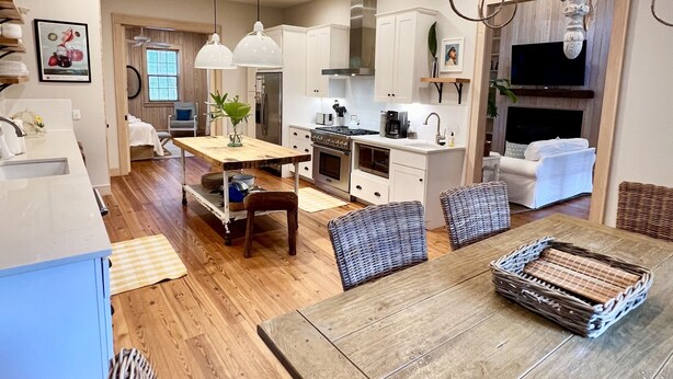 A modern kitchen with white cabinets, a wooden dining table, wicker chairs, and a chandelier. - Steps to Downtown, Pier & Beach with Gourmet Kitchen! (Folly Beach)