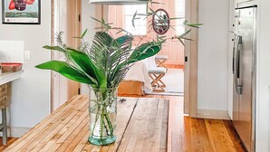 A modern kitchen with wooden flooring, white cabinets, a stainless steel refrigerator, and a large pendant light. - Steps to Downtown, Pier & Beach with Gourmet Kitchen! (Folly Beach)