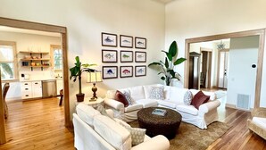 A spacious living room with wooden flooring, white sofas, a coffee table, and framed fish wall art. - Steps to Downtown, Pier & Beach with Gourmet Kitchen! (Folly Beach)
