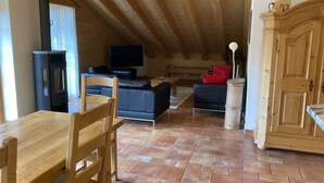 A cozy loft-style room with a wooden ceiling, a fireplace, a TV, and a dining area with a wooden table and chairs. - Fichte (Sulliger) by Interhome (Saanenmöser)