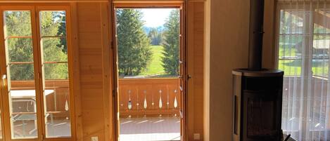 Ein Holzinnenraum mit Kamin, einer Schiebetür zu einem Balkon und Blick auf eine grüne Landschaft.