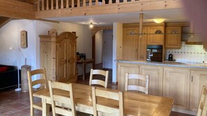 A wooden dining table with chairs, a kitchen with wooden cabinets, and a staircase leading to an upper level. - Fichte (Sulliger) by Interhome (Saanenmöser)