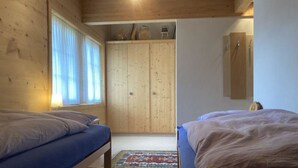 A room with two beds, wooden walls, a wardrobe, and a window. - Fichte (Sulliger) by Interhome (Saanenmöser)