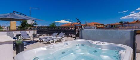 A rooftop pool area with a hot tub, lounge chairs, and umbrellas.