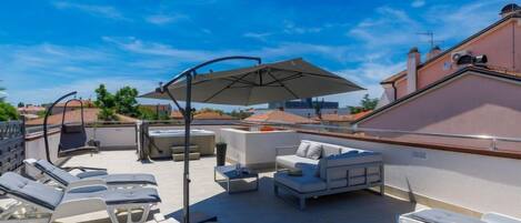 A rooftop terrace with lounge chairs, a sofa, and a hot tub.