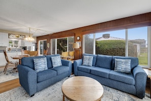 Relax in the spacious living room with a large sofa and dining area, offering a view of the outdoors.