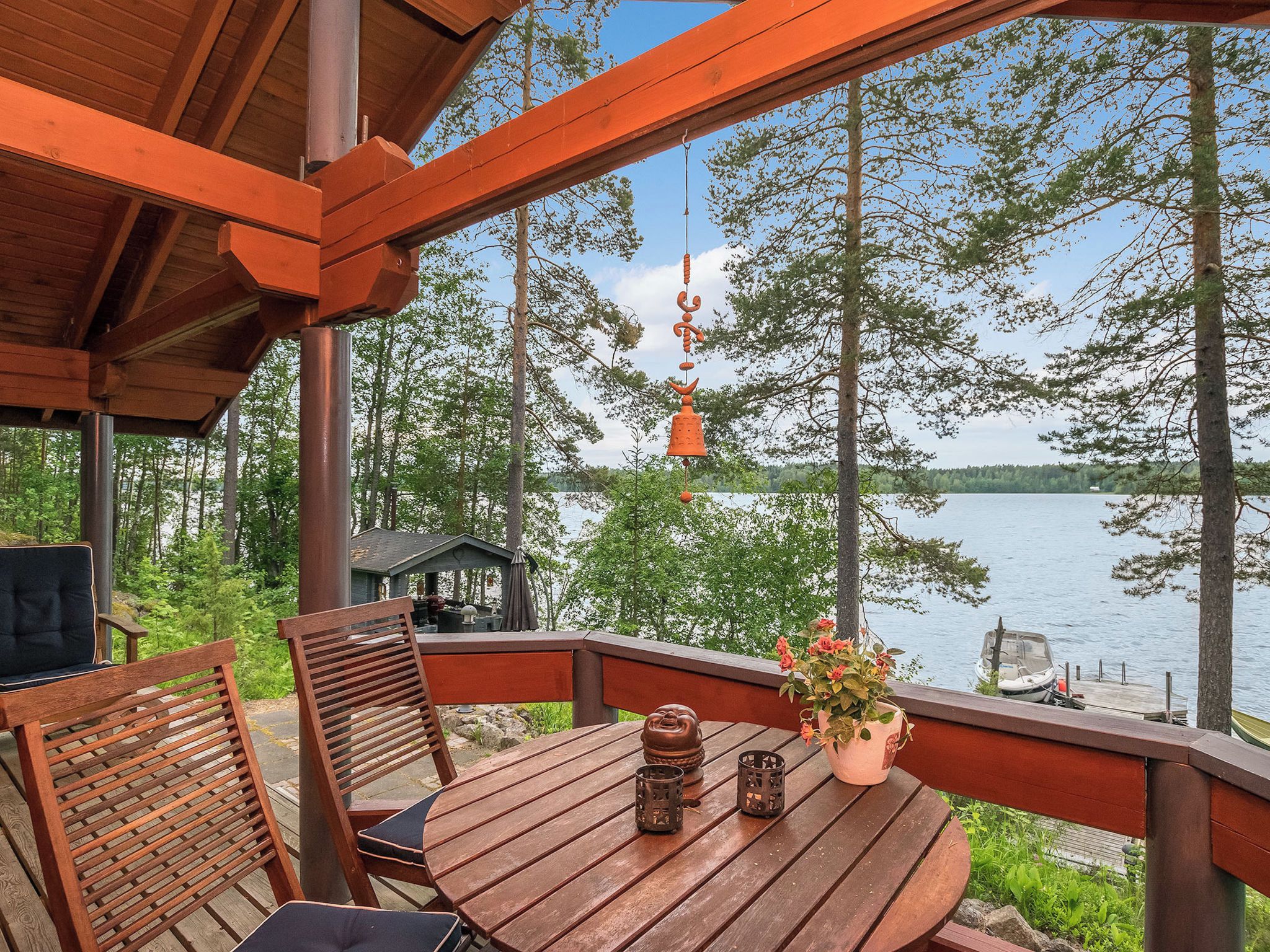 A wooden deck with a table and chairs, overlooking a lake with trees and a dock.