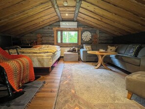 Um quarto de sótão acolhedor, com uma cama, um sofá, uma mesinha e um relógio na parede.