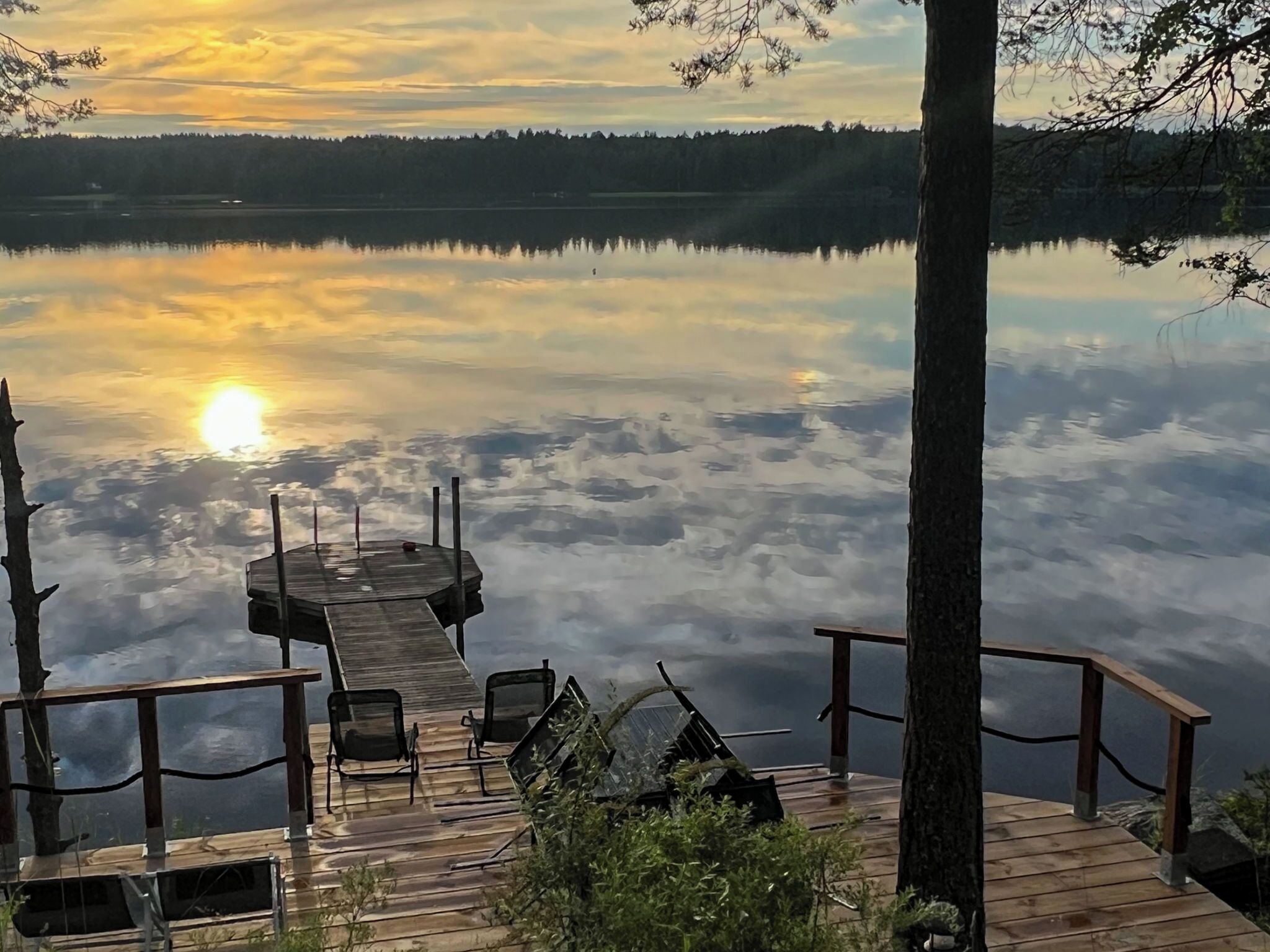 En träbrygga som sträcker sig ut i en stilla sjö, med en solnedgång i bakgrunden.