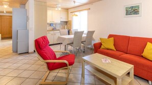 Un salon moderne avec un canapé rouge et un fauteuil rouge, une table basse en bois et un coin repas avec une table et des chaises blanches.