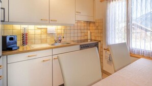 Une cuisine avec des meubles blancs, une cuisinière et un évier. Il y a une fenêtre avec des rideaux et une vue sur une maison à l’extérieur.