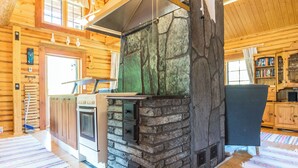 A rustic cabin interior with a stone fireplace, wooden walls, and a kitchen area. - Iltaranta by Interhome (Joutsa)