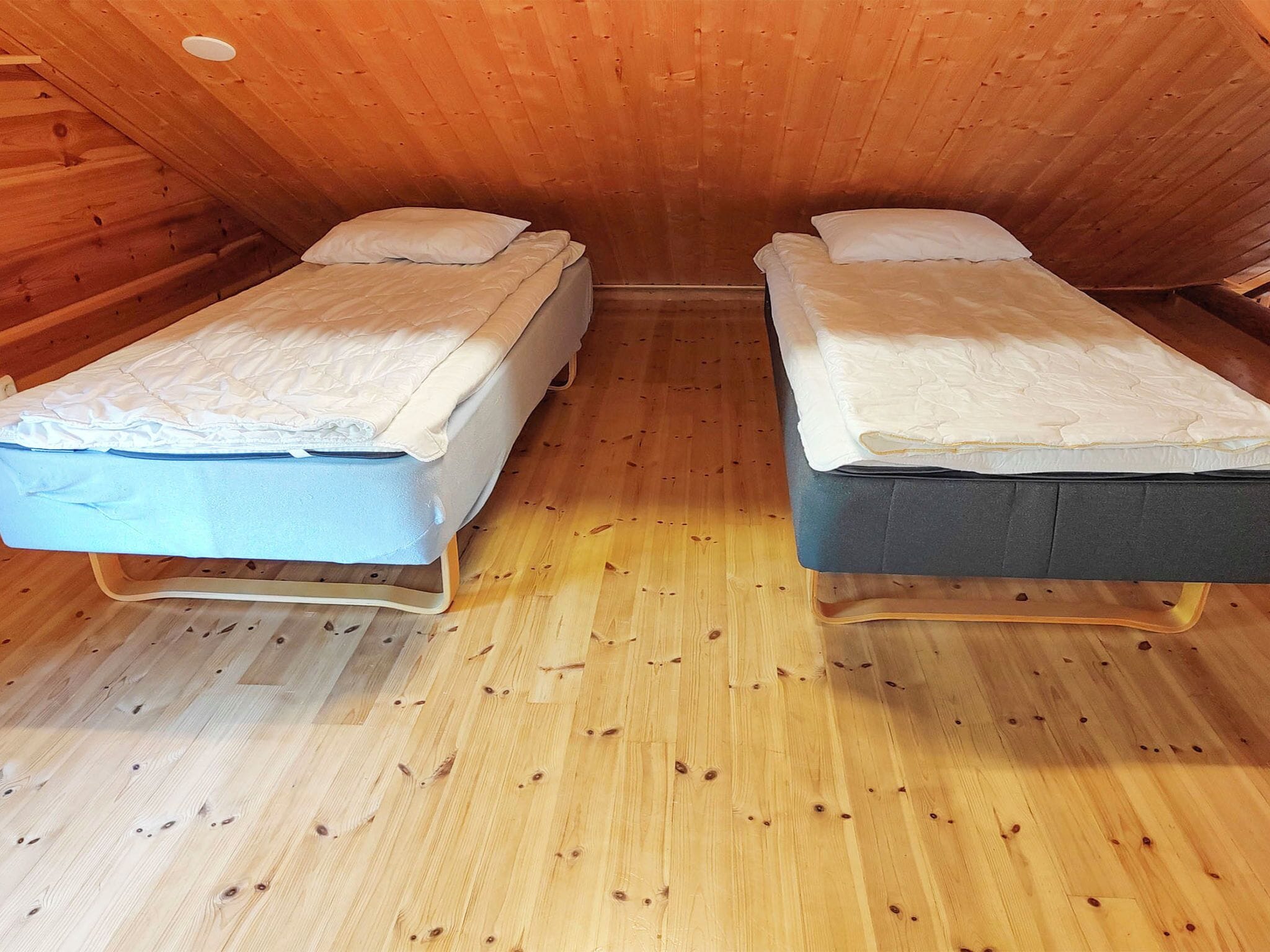 A small, cozy room with two single beds, wooden walls, and a wooden floor.