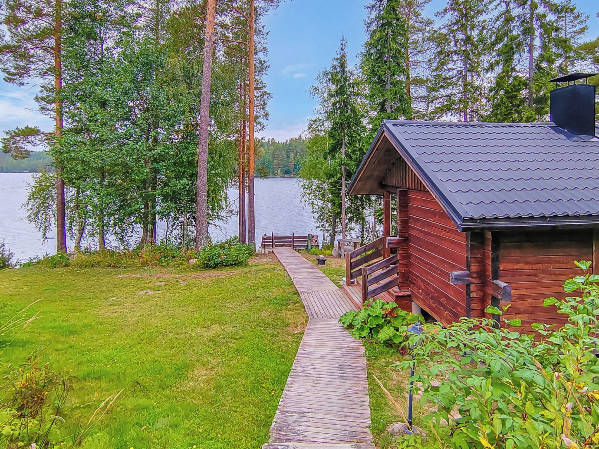 A cabin with a wooden deck leading to a dock by a lake, surrounded by tall trees.