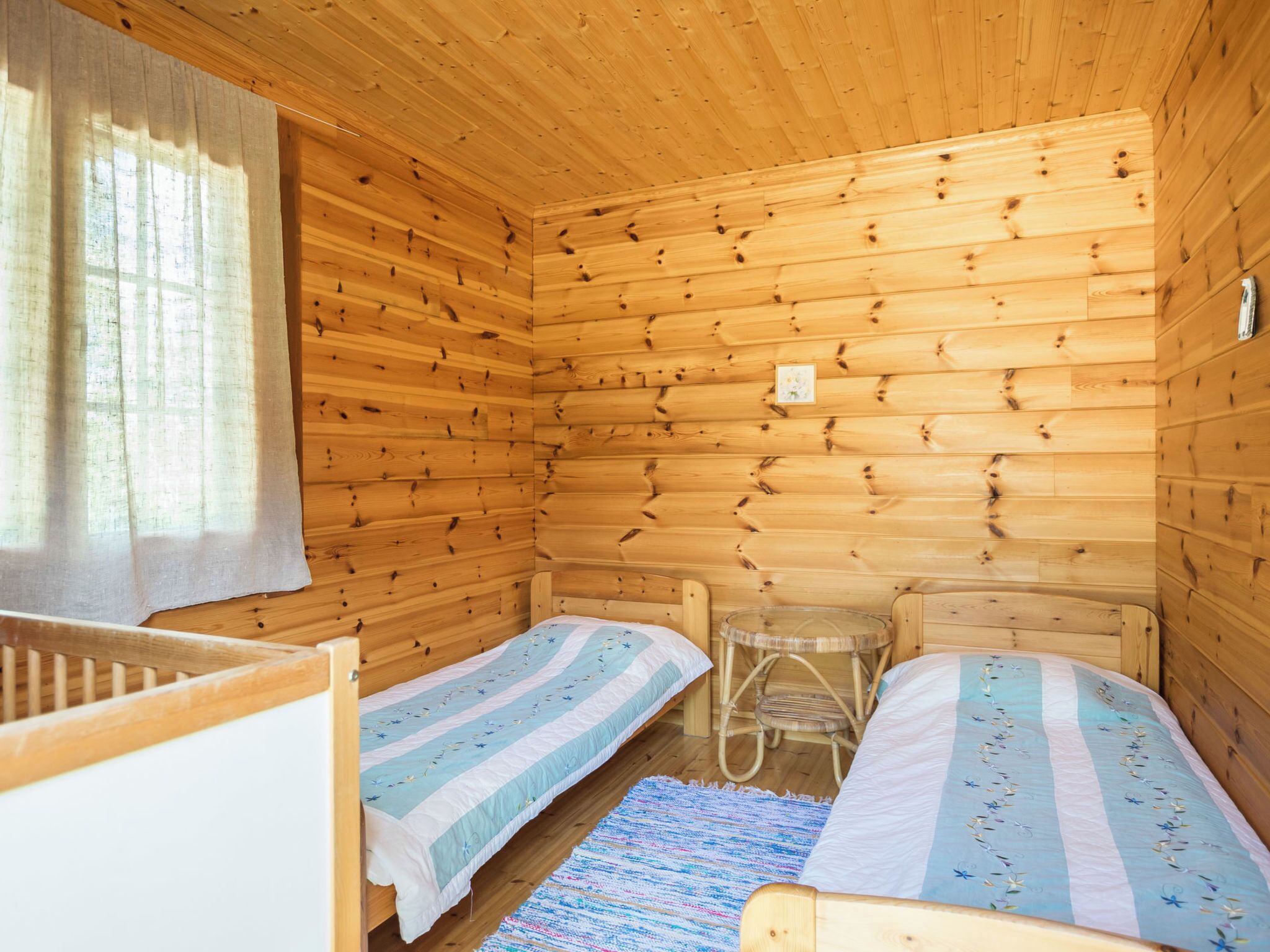 Una cabaña con dos literas de madera, una mesa pequeña y un ventanal con cortinas.
