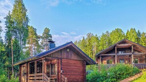A rustic cabin with a porch and a chimney, surrounded by lush greenery and tall trees. - Iltaranta by Interhome (Joutsa)