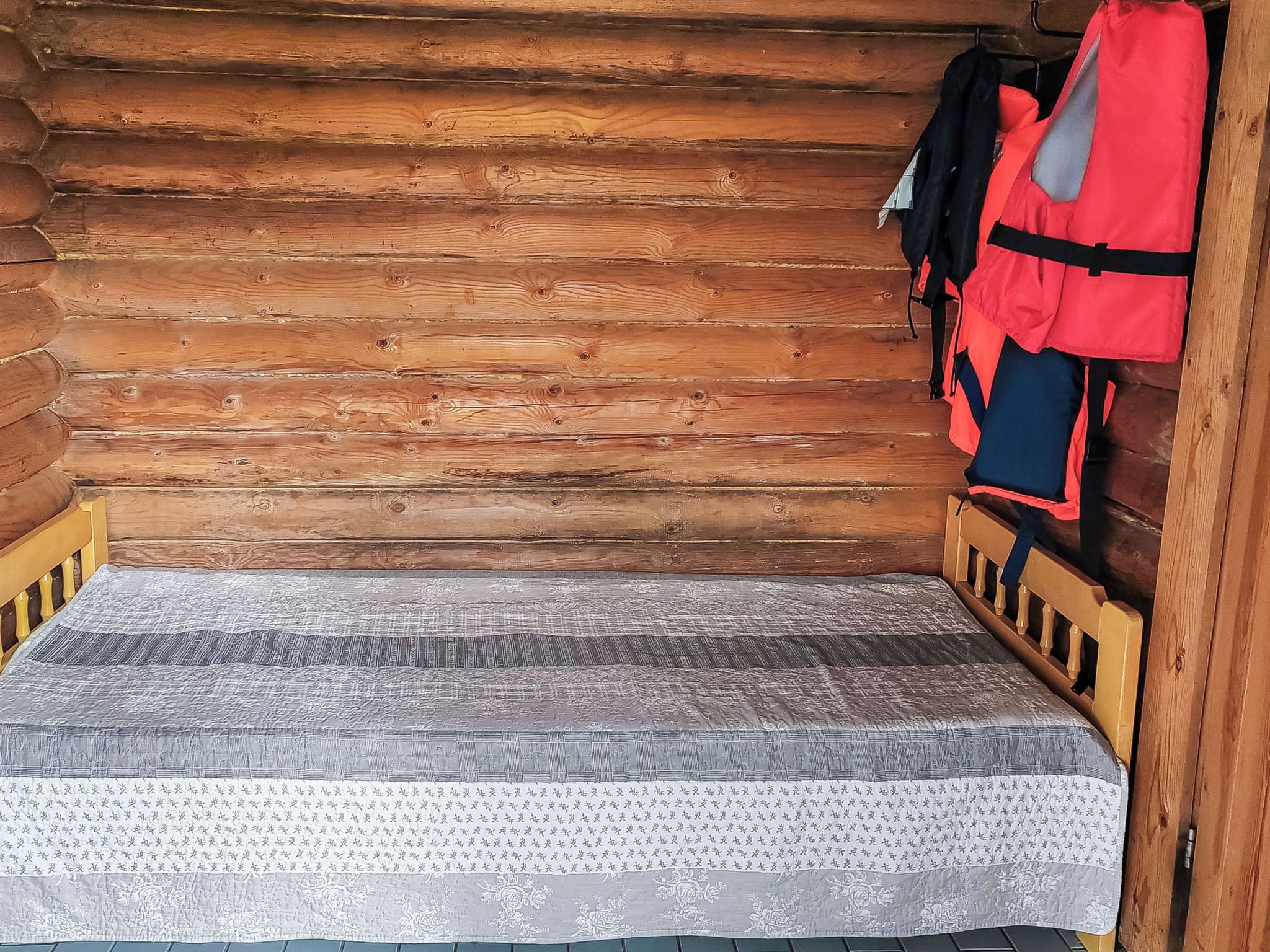A log cabin room with a single bed, a wooden headboard, and a mattress with a patterned cover.
