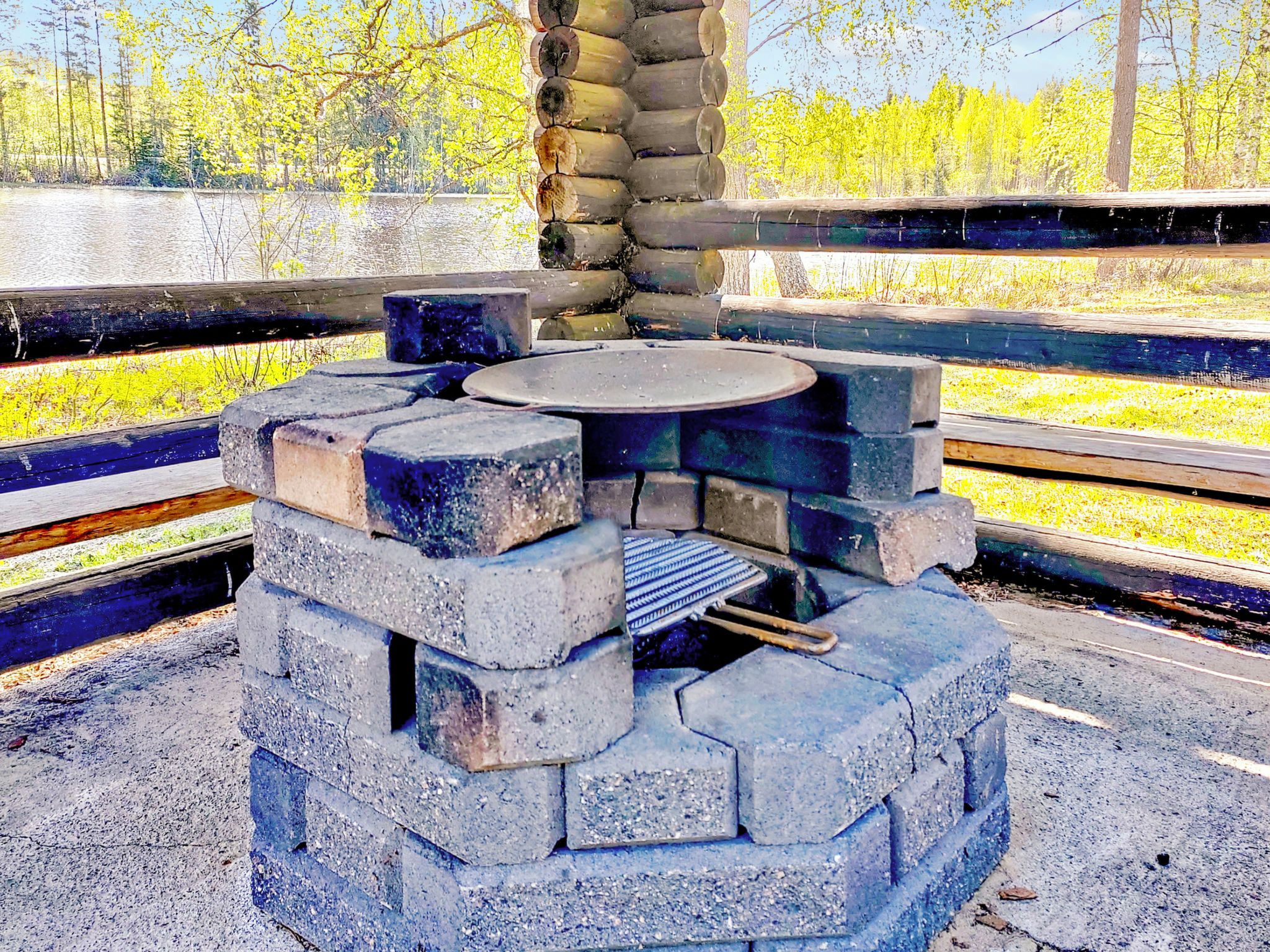 Zona de cuina exterior de pedra amb una graella circular i una reixa de metall, envoltada per una base de formigó i parets de pedra.